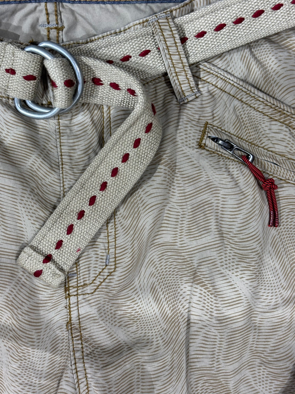 Close-up of a beige woven belt with red stitched dots, a silver metal ring, and a matching zip pocket on patterned khaki pants.